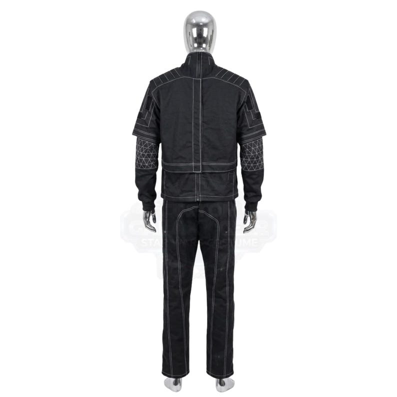 May include: A black tactical-style jacket and matching trousers set displayed on a mannequin. The jacket features a high collar, long sleeves with geometric white line patterns on the forearms, and prominent white stitching throughout the garment.