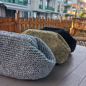 Peut inclure: Trois sacs tissés métalliques argentés, dorés et noirs sont disposés sur une surface grise. Les sacs ont une forme arrondie et un aspect texturé, suggérant une qualité artisanale. Les sacs sont exposés à l'extérieur.