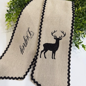 May include: Beige fabric banner with a black deer silhouette and the word "Degrey" embroidered in black. The banner has a scalloped black border. Decorative item.