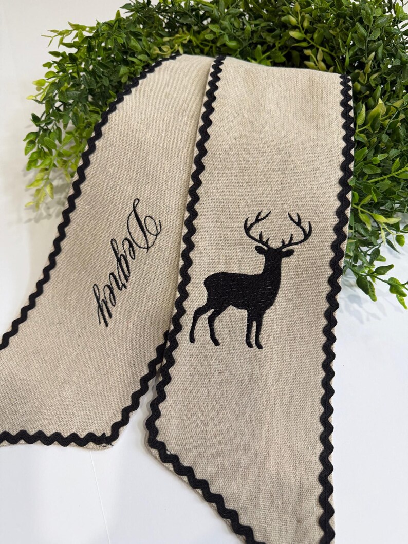 May include: Beige fabric banner with a black deer silhouette and the word "Degrey" embroidered in black. The banner has a scalloped black border. Decorative item.