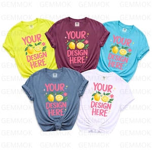 May include: Five short-sleeved crew neck t-shirts in neon yellow, maroon, light blue, slate blue, and white. Each shirt features a central graphic with the text "YOUR DESIGN HERE" in pink, accompanied by yellow lemon illustrations and small pink flowers.