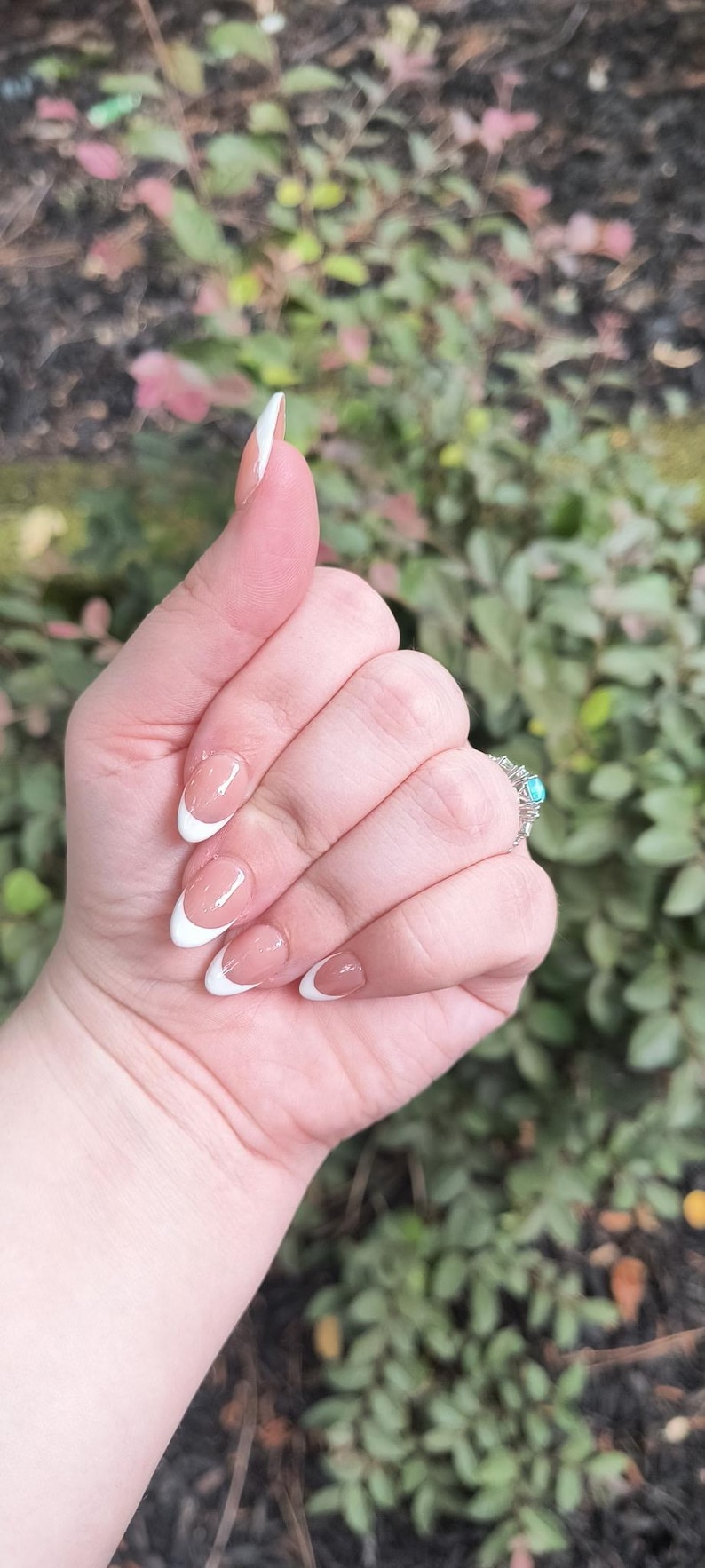 May include: Close-up of a hand with French tip acrylic nails. The nails are a natural pink with white tips. A silver ring with a turquoise stone is visible on the ring finger.