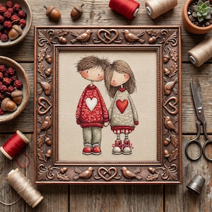 May include: A framed cross-stitch artwork depicts a couple holding hands, each wearing a sweater with a heart. The frame is bronze-colored with bird and heart motifs. Acorns, berries, and sewing supplies surround the frame on a wooden surface.
