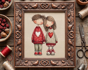 May include: A framed cross-stitch artwork depicts a couple holding hands, each wearing a sweater with a heart. The frame is bronze-colored with bird and heart motifs. Acorns, berries, and sewing supplies surround the frame on a wooden surface.