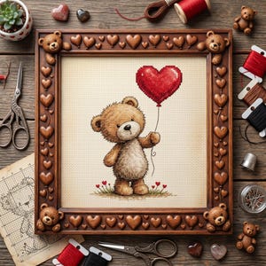Op de afbeelding: Een ingelijste kruissteek met een teddybeer die een rode hartvormige ballon vasthoudt. De bruine houten lijst is versierd met hart- en teddybeeraccenten. Naaibenodigdheden omringen de afbeelding.