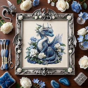 May include: A framed cross-stitch of a blue dragon surrounded by white and blue flowers. The silver frame is adorned with dragon sculptures. Additional dragon figurines, embroidery floss, scissors, and flowers are arranged on a wooden surface.