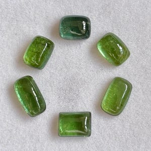Puede incluir: Seis piedras preciosas verdes rectangulares pulidas dispuestas en un patrón circular. Cada piedra presenta una superficie lisa estilo cabujón con variadas inclusiones internas y un color verde lima translúcido y vibrante.