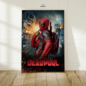 May include: A framed poster featuring Deadpool in a red and black costume, standing in a city setting with a backpack. The word "DEADPOOL" is prominently displayed in red at the bottom. The background includes buildings and a fiery sky.