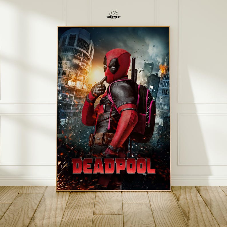 May include: A framed poster featuring Deadpool in a red and black costume, standing in a city setting with a backpack. The word "DEADPOOL" is prominently displayed in red at the bottom. The background includes buildings and a fiery sky.