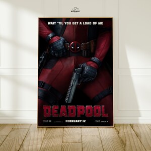 May include: A framed movie poster for Deadpool. The poster features the character in a red suit, holding a gun. The title "DEADPOOL" is in large red letters at the bottom, with the release date "FEBRUARY 12" below it. The text "WAIT 'TIL YOU GET A LOAD OF ME" is at the top.