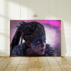 May include: A framed print featuring a portrait of a person with blue face paint and a fur-lined garment. The person is wearing a decorated headpiece. The background has a purple and pink gradient. The Wildwest logo is in the top right corner.