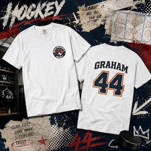May include: Two white t-shirts with hockey designs. One has a small logo, the other displays "GRAHAM" and the number "44". The background features hockey-related graphics and text, including "Leave it all on the ice."