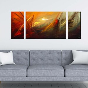 May include: A three-piece abstract art print set featuring a vibrant orange, yellow, and red color scheme. The artwork depicts a dynamic, swirling pattern with a hint of white in the center. The prints are displayed on a gray sofa in a modern living room setting.