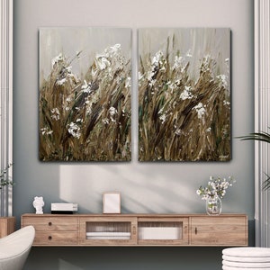 May include: A living room interior design with a white armchair and ottoman, two white side tables, a wooden media console, and two abstract paintings of white flowers on a brown background.