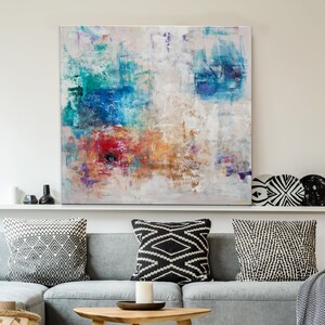 May include: A gray sectional sofa with black and white patterned throw pillows, a wooden coffee table, a woven basket, and a woven ottoman. An abstract painting with blue, green, red, and orange hues hangs above the sofa.