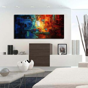 May include: Abstract painting with a mix of blue, green, orange, and red colors. The painting is displayed on a white wall above a white couch with pillows.
