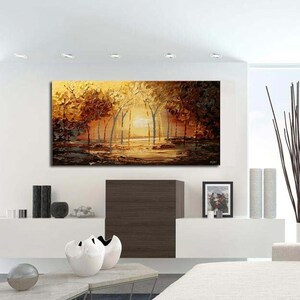 May include: A painting of a forest scene with trees in shades of brown and yellow. The trees are reflected in a still body of water in the foreground. The painting is displayed on a white wall above a white couch with pillows.