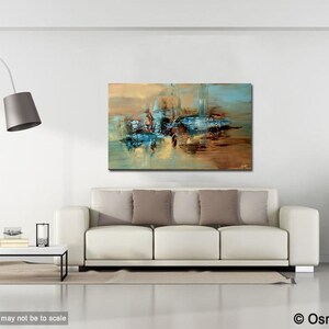 May include: Abstract painting with blue, brown, and gold hues. The painting is hanging on a white wall above a white couch with brown pillows.