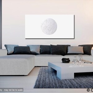 May include: White textured canvas painting with a large white circle in the center. The painting is hanging on a white wall above a gray sectional sofa with black pillows. A white coffee table sits in front of the sofa.