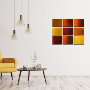 May include: A modern living room interior with a yellow armchair, a coffee table, and a wall art piece featuring a grid of 12 abstract squares in shades of orange, red, and yellow.