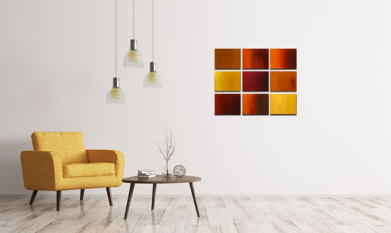 May include: A modern living room interior with a yellow armchair, a coffee table, and a wall art piece featuring a grid of 12 abstract squares in shades of orange, red, and yellow.