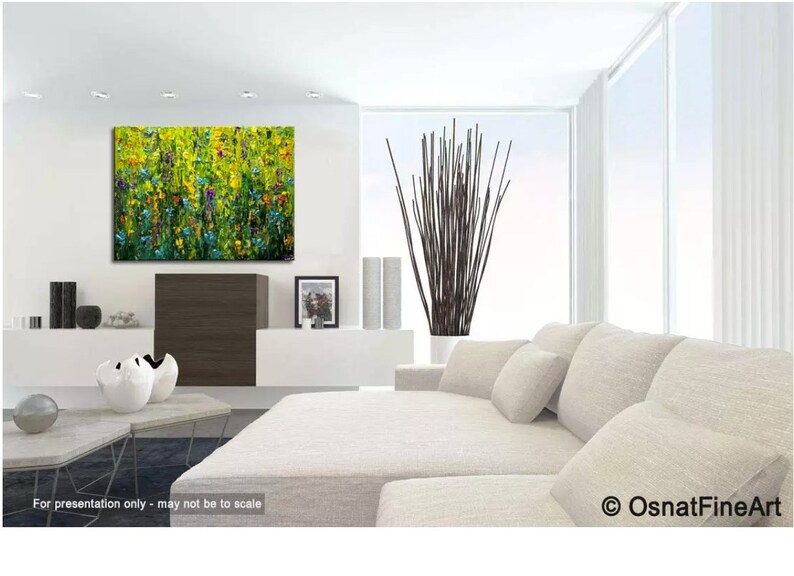 May include: An abstract painting of a field of flowers in shades of yellow, green, blue, and purple hangs on a white wall. The living room features a white sofa, modern decor, and a large window. The artwork is signed by OsnatFineArt.