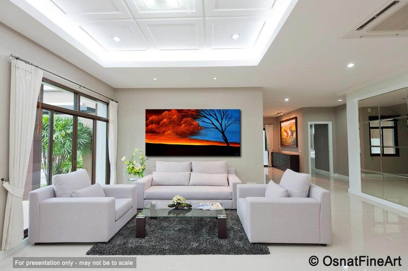 May include: A large abstract painting of a sunset with a tree in the foreground. The sky is a mix of orange, red, and blue. The tree is silhouetted against the sky. The painting is hanging on a wall in a living room.
