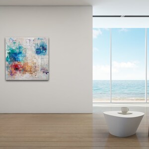 May include: Abstract painting with blue, red, orange, and yellow colors on a white background. The painting is hanging on a white wall in a modern room with a large window overlooking the ocean.