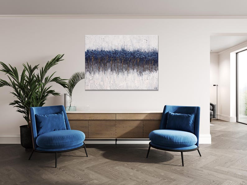 May include: Abstract art piece with a textured white background and a horizontal band of dark blue and gold tones. The artwork hangs above a wooden cabinet, flanked by two blue armchairs.
