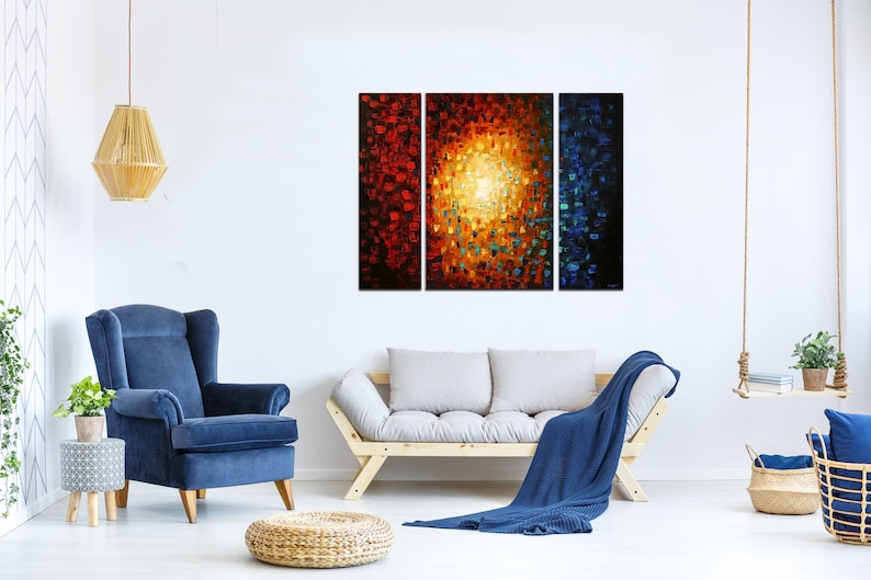 May include: A three-piece abstract painting with a bright yellow center surrounded by red, orange, and blue hues. The painting is displayed on a white wall above a couch and a chair.
