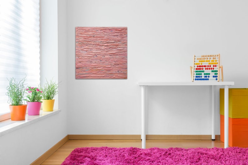 May include: A pink abstract painting with horizontal brushstrokes hangs on a white wall above a white desk with a wooden abacus. The desk is in a room with a window and a pink rug.