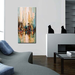 May include: Abstract painting of a city skyline in shades of blue, green, yellow, and brown. The painting is on a canvas and is framed. The painting is hanging on a white wall in a living room.