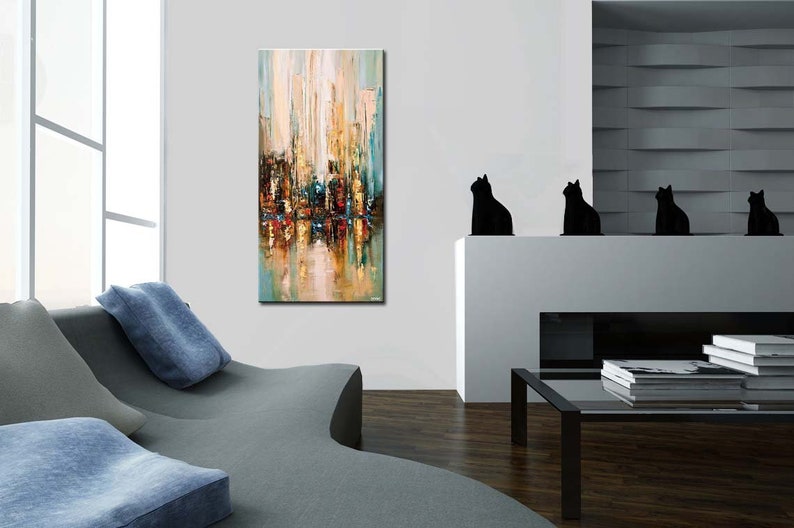 May include: Abstract painting of a city skyline in shades of blue, green, yellow, and brown. The painting is on a canvas and is framed. The painting is hanging on a white wall in a living room.