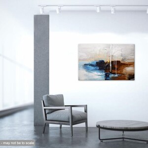 May include: Abstract painting with blue, brown, and white paint on a canvas. The painting is hanging on a white wall in a modern living room setting.