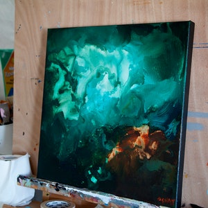 May include: Abstract painting on canvas with swirling green, blue, and brown colours. The painting is on an easel and has a black frame.