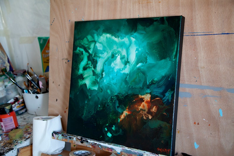 May include: Abstract painting on canvas with swirling green, blue, and brown colours. The painting is on an easel and has a black frame.
