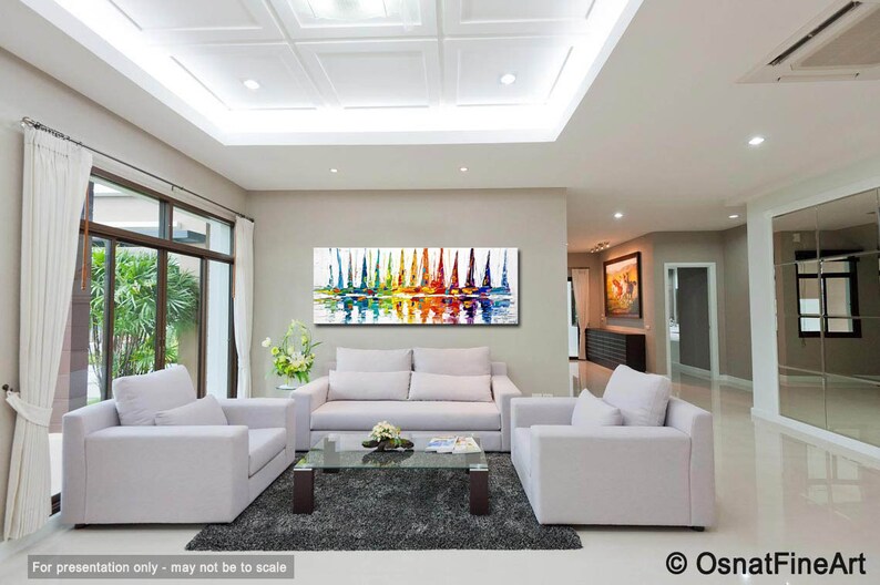 May include: Abstract painting of colorful sailboats on a white background with a reflection in the water. The painting is displayed in a living room with white furniture and a gray rug.