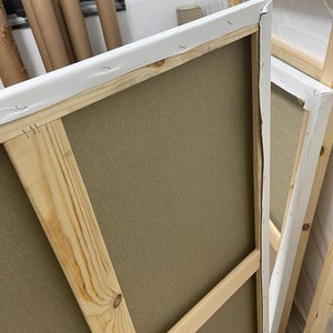 May include: A wooden canvas frame with a beige canvas stretched over it. The frame is made of natural wood and has a white fabric border.