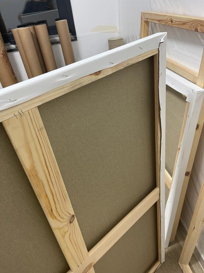 May include: A wooden canvas frame with a beige canvas stretched over it. The frame is made of natural wood and has a white fabric border.