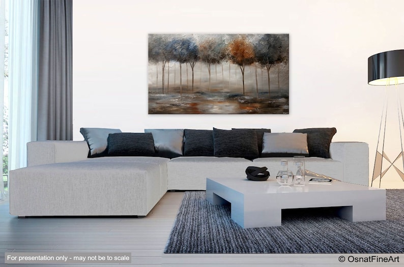 May include: Abstract painting of a forest scene with trees in shades of blue, brown, and gray. The trees are silhouetted against a misty background. The painting is displayed on a wall in a living room setting.