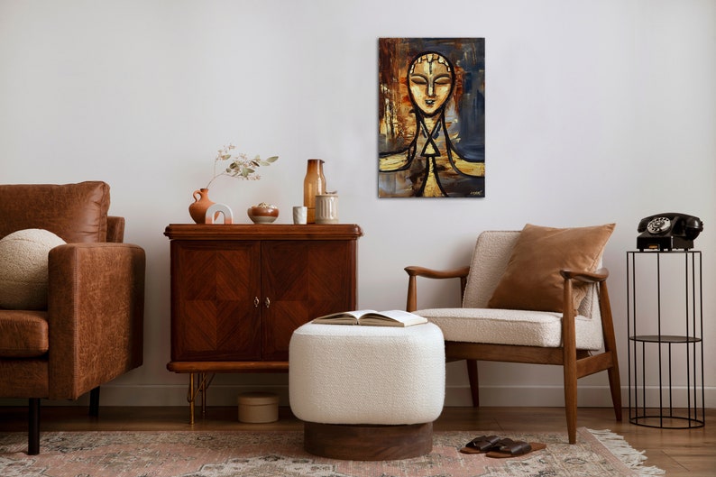 May include: A painting of a stylized human face with a golden background and blue accents. The painting is framed and hanging on a white wall in a living room setting.