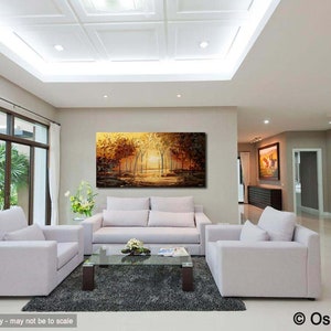 May include: A living room interior with a large abstract painting of a forest scene in shades of gold, brown, and green. The painting is hanging on a wall above a white sofa. There are two white armchairs in the room, and a coffee table with a glass top.