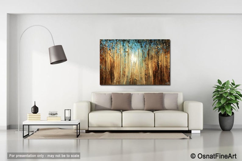 May include: Abstract painting of a forest scene with a blue and gold color scheme. The painting is hanging on a white wall above a white couch with brown pillows.