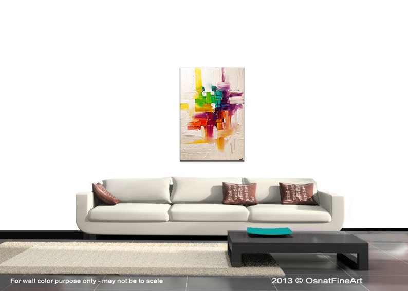 May include: Abstract painting with a white background and colorful geometric shapes in shades of yellow, orange, red, green, purple, and blue. The painting is displayed on a white wall above a white couch with brown pillows.