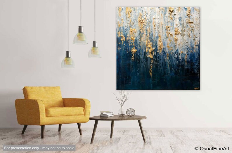 May include: Abstract textured painting with gold and navy blue tones. The artwork features vertical brushstrokes and a layered effect, creating a sense of depth. The painting is displayed in a modern living room setting with a yellow armchair and a round coffee table.