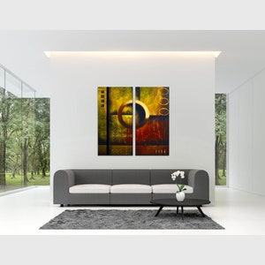 May include: Abstract art print in a modern living room setting. The print is a two-piece set with a yellow, orange, and brown color scheme. The print is hanging on a white wall above a gray couch.