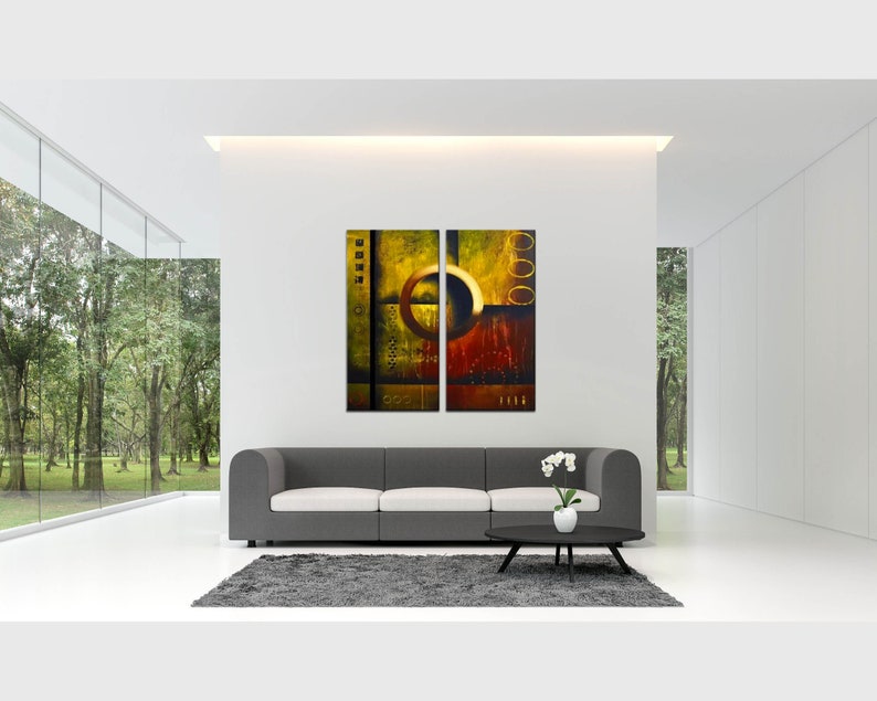 May include: Abstract art print in a modern living room setting. The print is a two-piece set with a yellow, orange, and brown color scheme. The print is hanging on a white wall above a gray couch.
