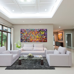 May include: A living room interior with white walls and a white ceiling. There is a large abstract painting on the wall with splashes of red, yellow, blue, green, and purple paint. The room has a white sofa, two white armchairs, a glass coffee table, and a gray rug.