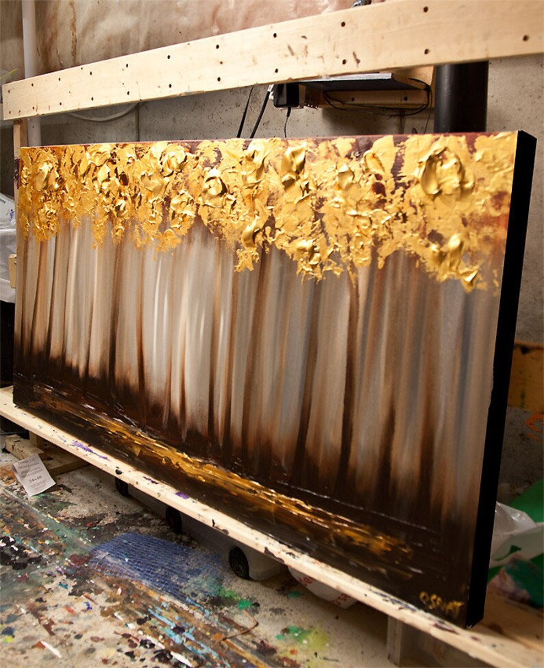 May include: Abstract painting of a forest scene with gold leaf accents. The painting is on a canvas with a black frame.