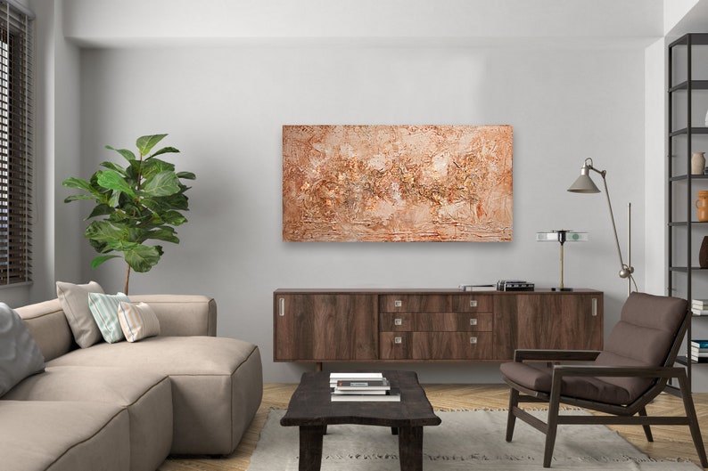 May include: Abstract textured painting in shades of brown and beige, mounted on a wall above a dark wood cabinet. The artwork is the focal point of a modern living room, complemented by a sectional sofa, a wooden chair, and a coffee table.